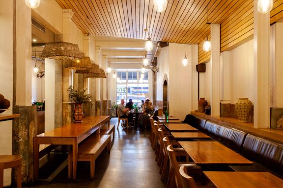 Inside Loretta's, a casual café on Cuba Street in Te Aro Wellington. There are wooden tables and chairs, benches and a group of people eating at a table in the background. 