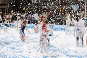 Image of children playing in a paddling pool filled with white foam. Some of the foam bubbles are airborne, giving the impression it's snowing.