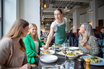 Waiter serves a plate of food to customers seated at a table in Charley Noble.