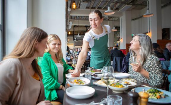 Waiter serves a plate of food to customers seated at a table in Charley Noble.