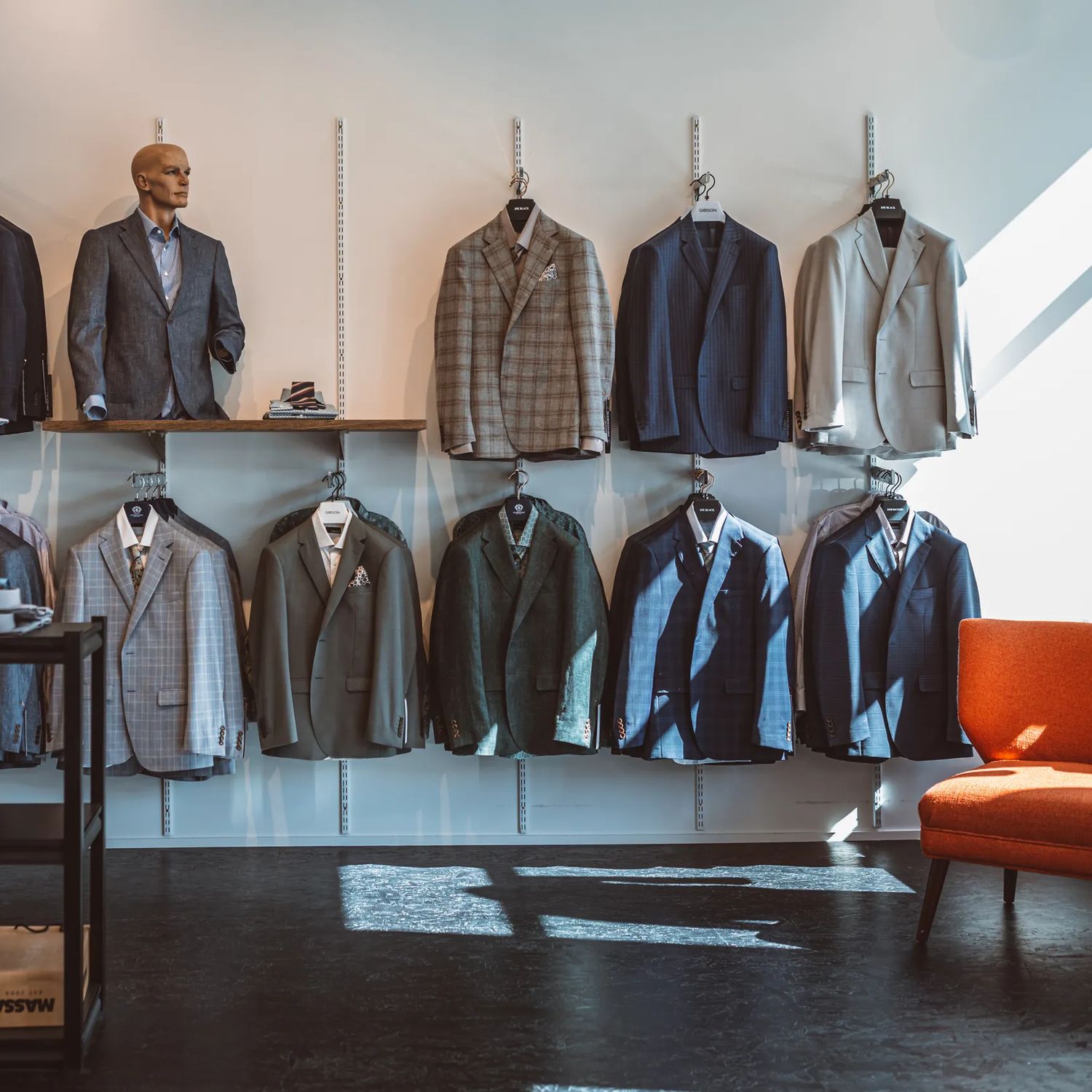 Inside Mandatory Menswear Ltd, a men's clothing store in Te Aro, Wellington. The modern space has white walls, black floors, suit jackets hanging against the wall and a mannequin.