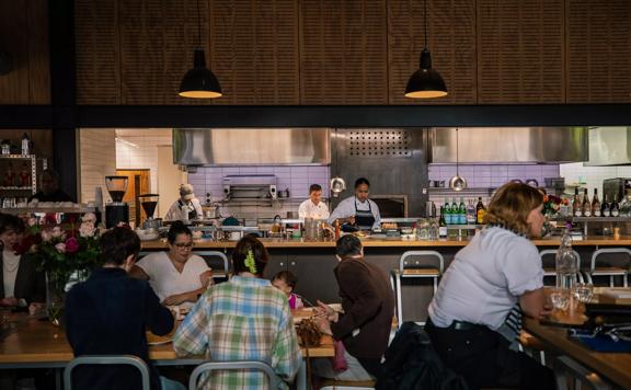 The interior of Prefab Eatery, a restaurant in Te Aro Wellington. There is an open kitchen and the tables are occupied by happy diners. 