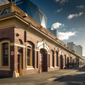 The exterior of the New Zealand Portrait Gallery — a historic brick shed on the waterfront, with city buildings behind it.