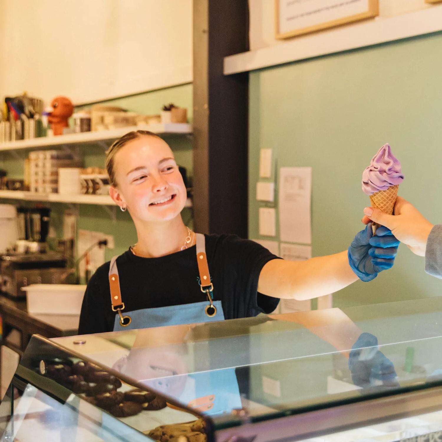 A Zelati employee gives an ube soft serve to a customer.