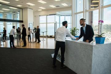 The Cliftons lobby, a member of staff stands behind a large marble table and shakes hands with a person in a suit, and others in suits stand in the background around tables talking to each other.