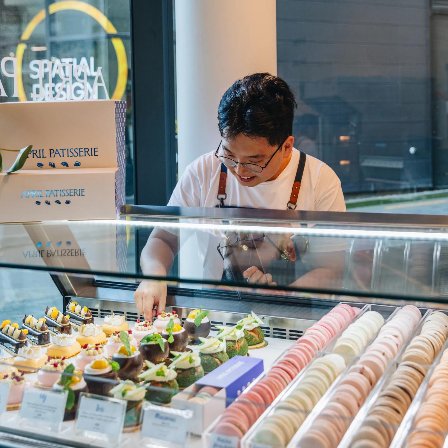 A staff member arranges desserts in the display case at April Patisserie.