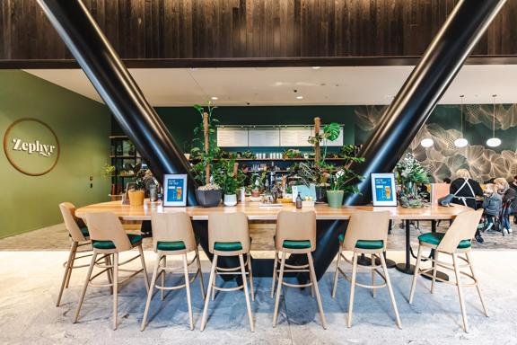 A high table at Zephyr café  in Tākina, with plants placed in the centre. The green wall and accents give the cafe a nature feeling.