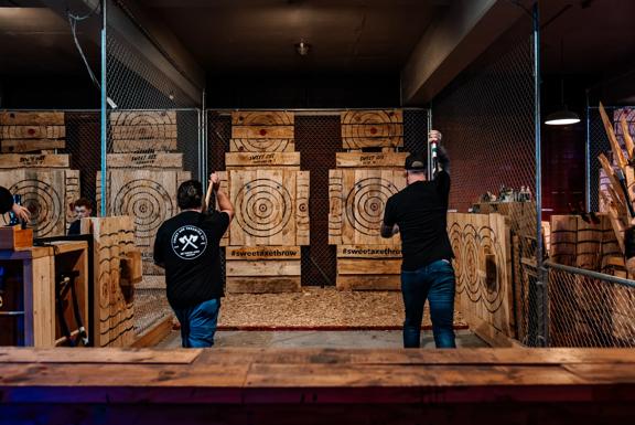 Two people prepare to throw axes at wooden targets at Sweet Axe Throwing. Metal fences line the throwing area.
