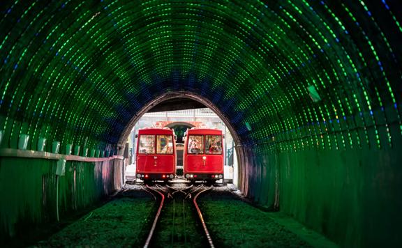 Looking into the Cable Car tunnel, with green LED lights lighting the inside and the 2 Cable cars meet in the middle of the tracks side by side.