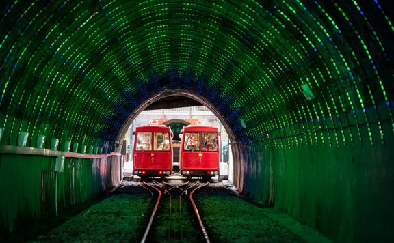 Looking into the Cable Car tunnel, with green LED lights lighting the inside and the 2 Cable cars meet in the middle of the tracks side by side.