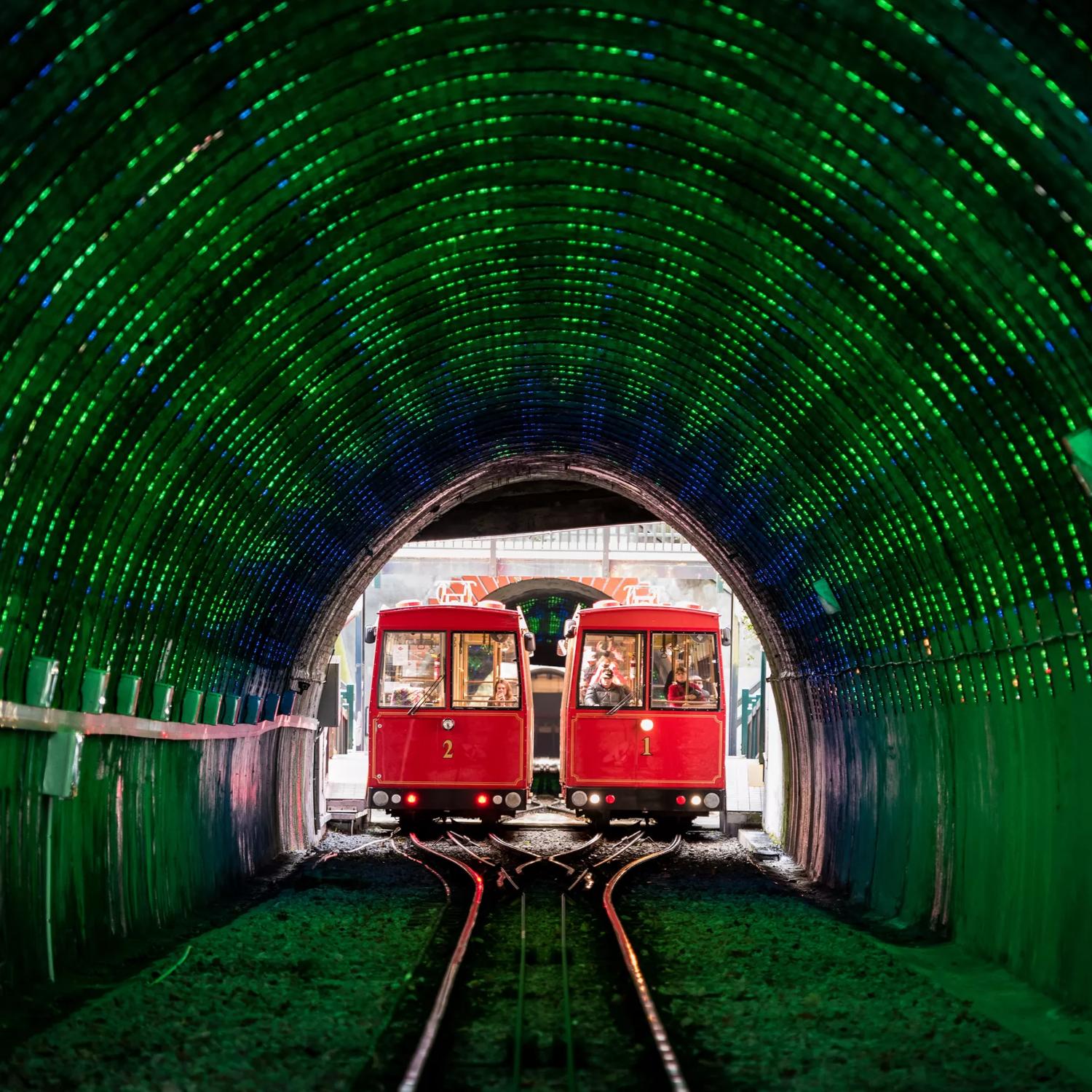 Looking into the Cable Car tunnel, with green LED lights lighting the inside and the 2 Cable cars meet in the middle of the tracks side by side.