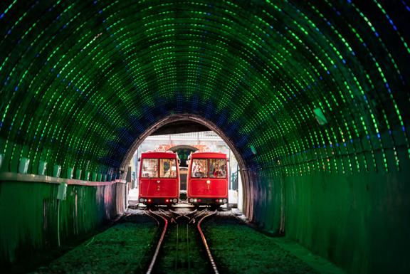 Looking into the Cable Car tunnel, with green LED lights lighting the inside and the 2 Cable cars meet in the middle of the tracks side by side.