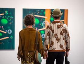 Two people standing next to one another, holding hands, admiring an artwork at the City Gallery Wellington Te Whare Toi. 