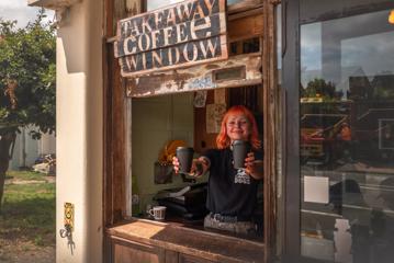 A waiter hands coffees through a window at Raumati Social Club.