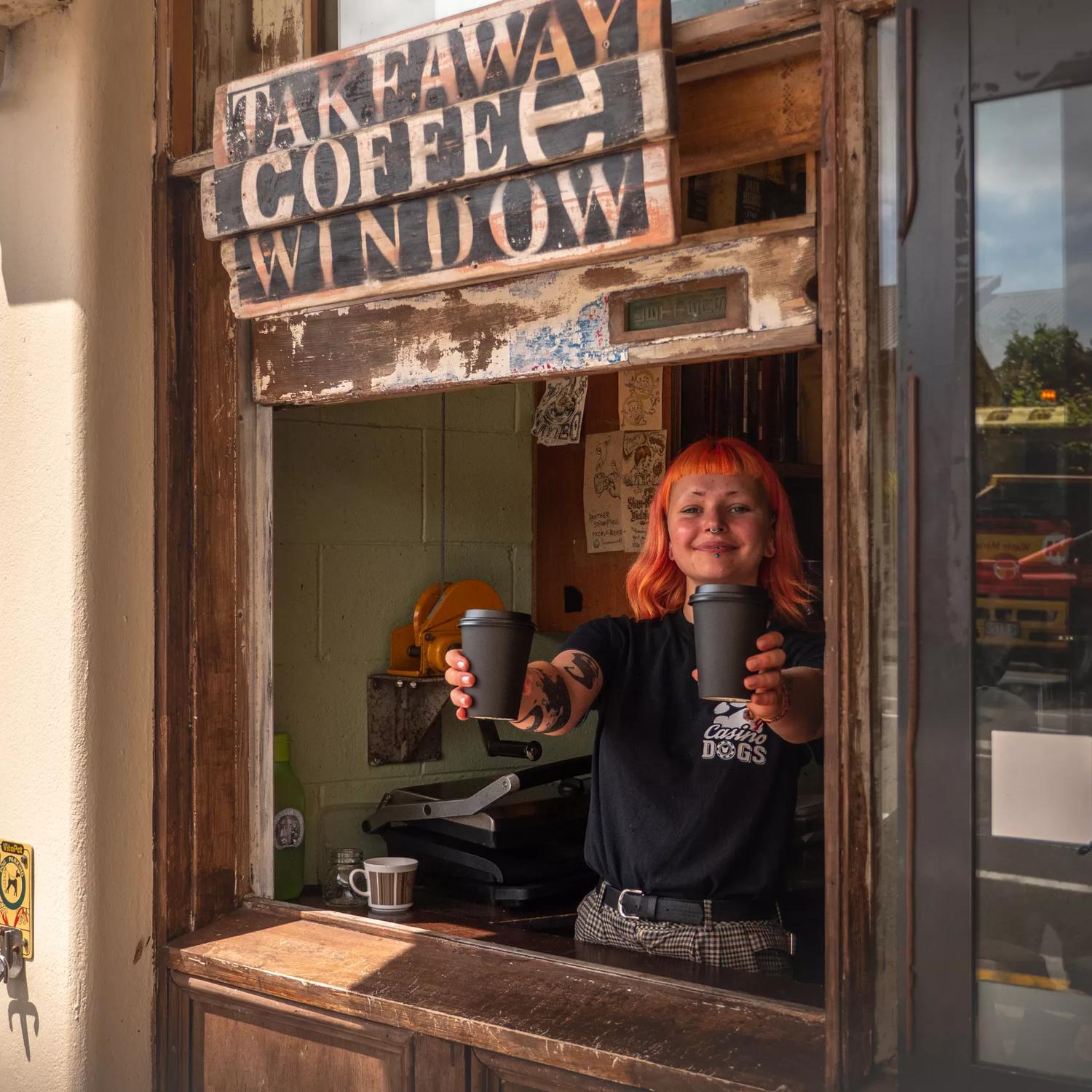A waiter hands coffees through a window at Raumati Social Club.