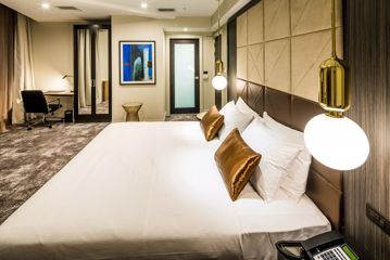 A King bedroom at the Doubletree by Hilton, the bed has crisp white linen with bronze cushions against a leather headboard. Gold pendant lights hang on either side of the bed.