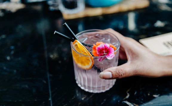 A gin-based cocktail with a dried orange slice and pink flower garnish.
