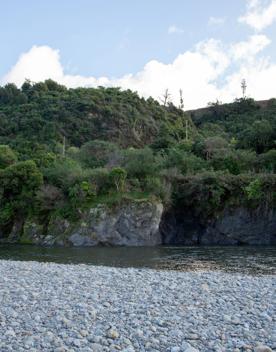 The Taitā Rock swimming hole in Lower Hutt, with lush green bush surrounding a blue river and large pebbles on the shore.