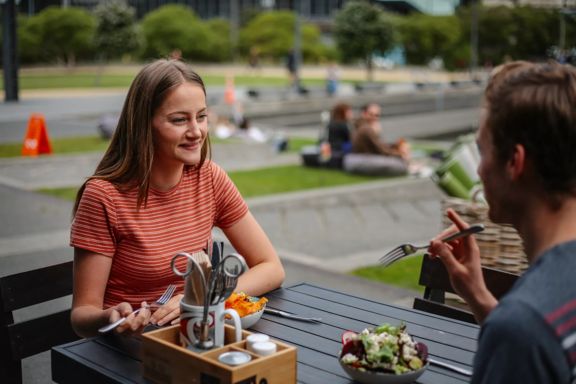 A happy couple eats lunch on the patio at Karaka Café at Te Wharewaka o Pōneke.