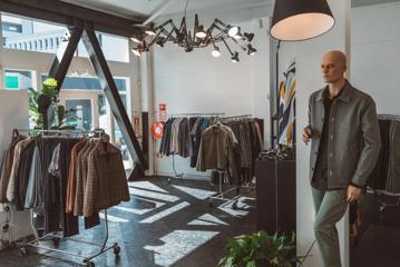 Inside Mandatory Menswear Ltd, a men's clothing store in Te Aro, Wellington. The modern space has white walls, black floors, a mannequin and clothing on hangers.