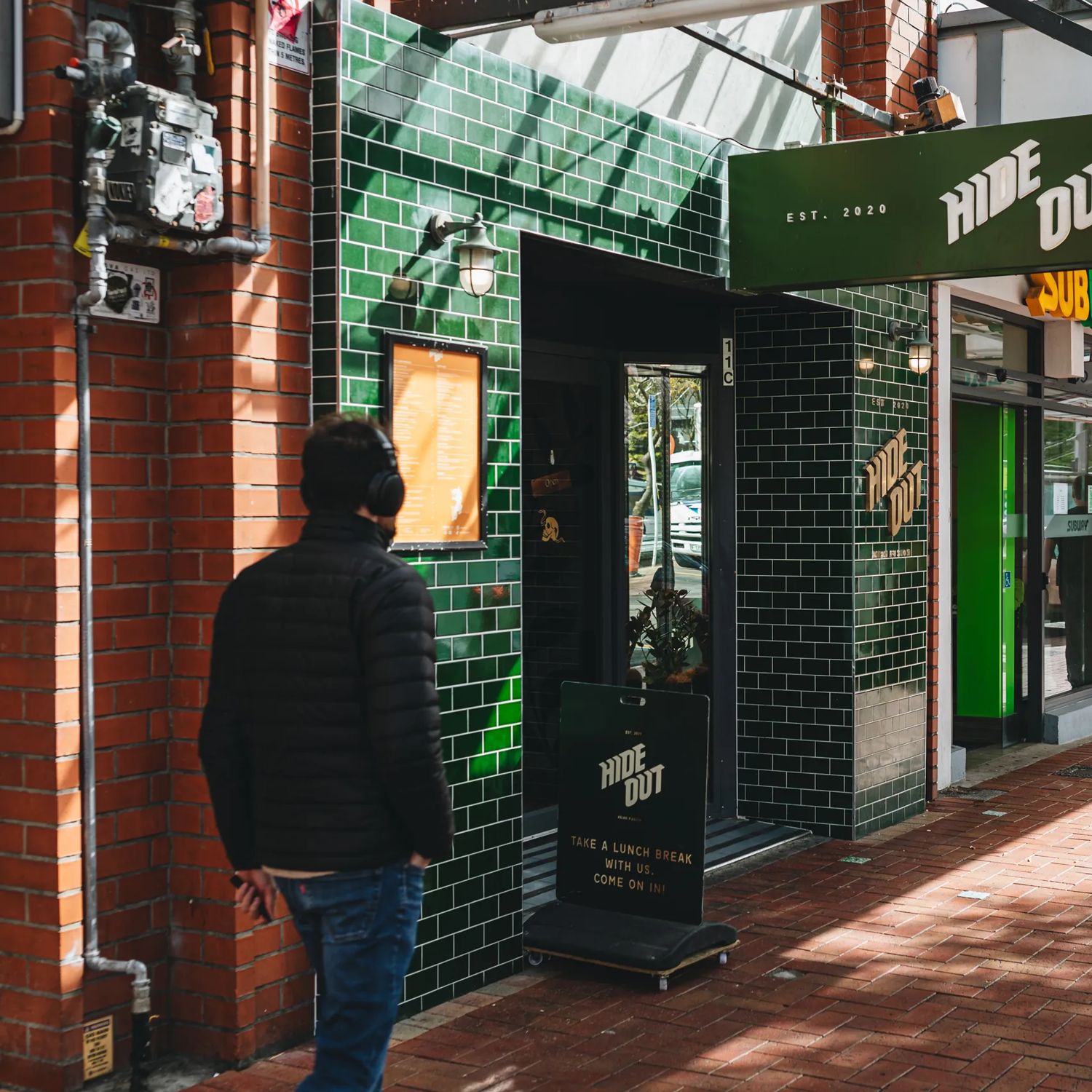 The front facade of Hideout, a pan-Asian restaurant on Courtenay Place in Te Aro Wellington. The wall is made of dark green subway tiles facing a covered red-brick sidewalk.