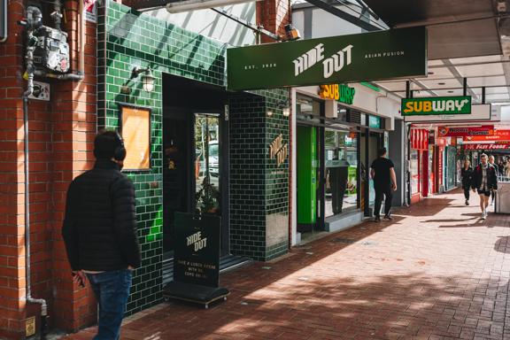 The front facade of Hideout, a pan-Asian restaurant on Courtenay Place in Te Aro Wellington. The wall is made of dark green subway tiles facing a covered red-brick sidewalk. 