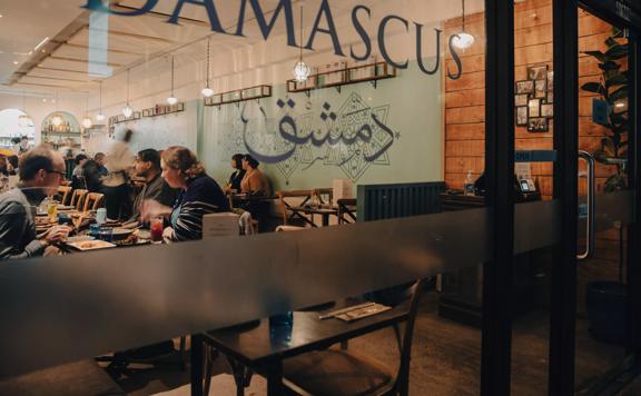 The glass door of Damascus with their logo printed on the inside. Customers enjoy their meals inside.