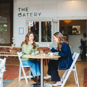 Two people sit at a table outside The Oatery in Left Bank. They are both eating from a bowl.