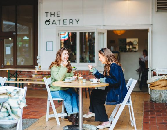 Two people sit at a table outside The Oatery in Left Bank. They are both eating from a bowl.