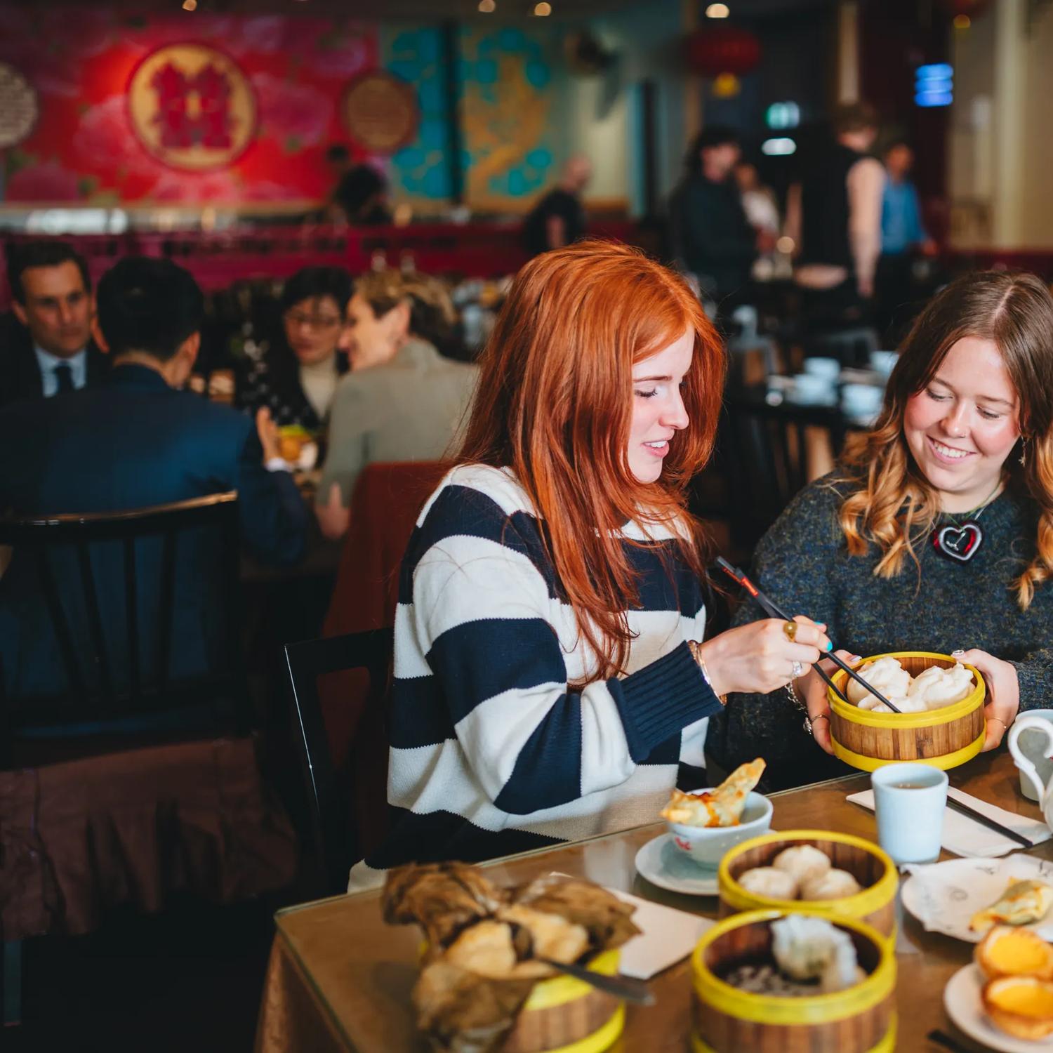 Two friends enjoy yum cha at Dragons Chinese restaurant. There is an array of dishes, two cups and a teapot on the table.