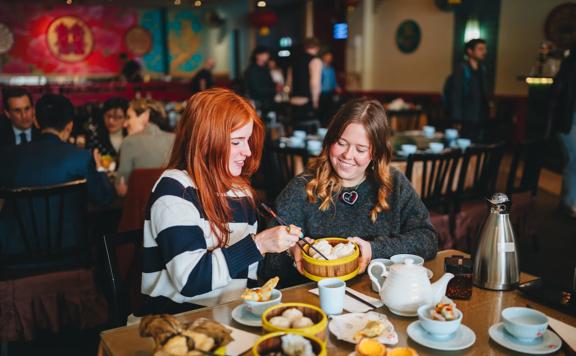 Two friends enjoy yum cha at Dragons Chinese restaurant. There is an array of dishes, two cups and a teapot on the table.