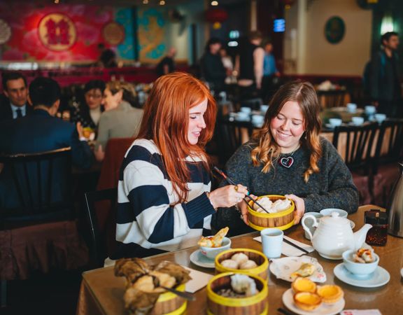 Two friends enjoy yum cha at Dragons Chinese restaurant. There is an array of dishes, two cups and a teapot on the table.