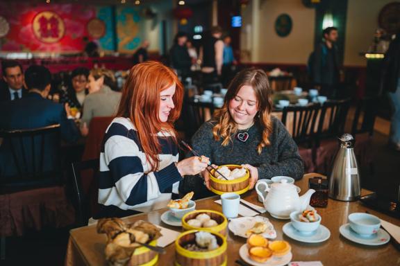 Two friends enjoy yum cha at Dragons Chinese restaurant. There is an array of dishes, two cups and a teapot on the table.