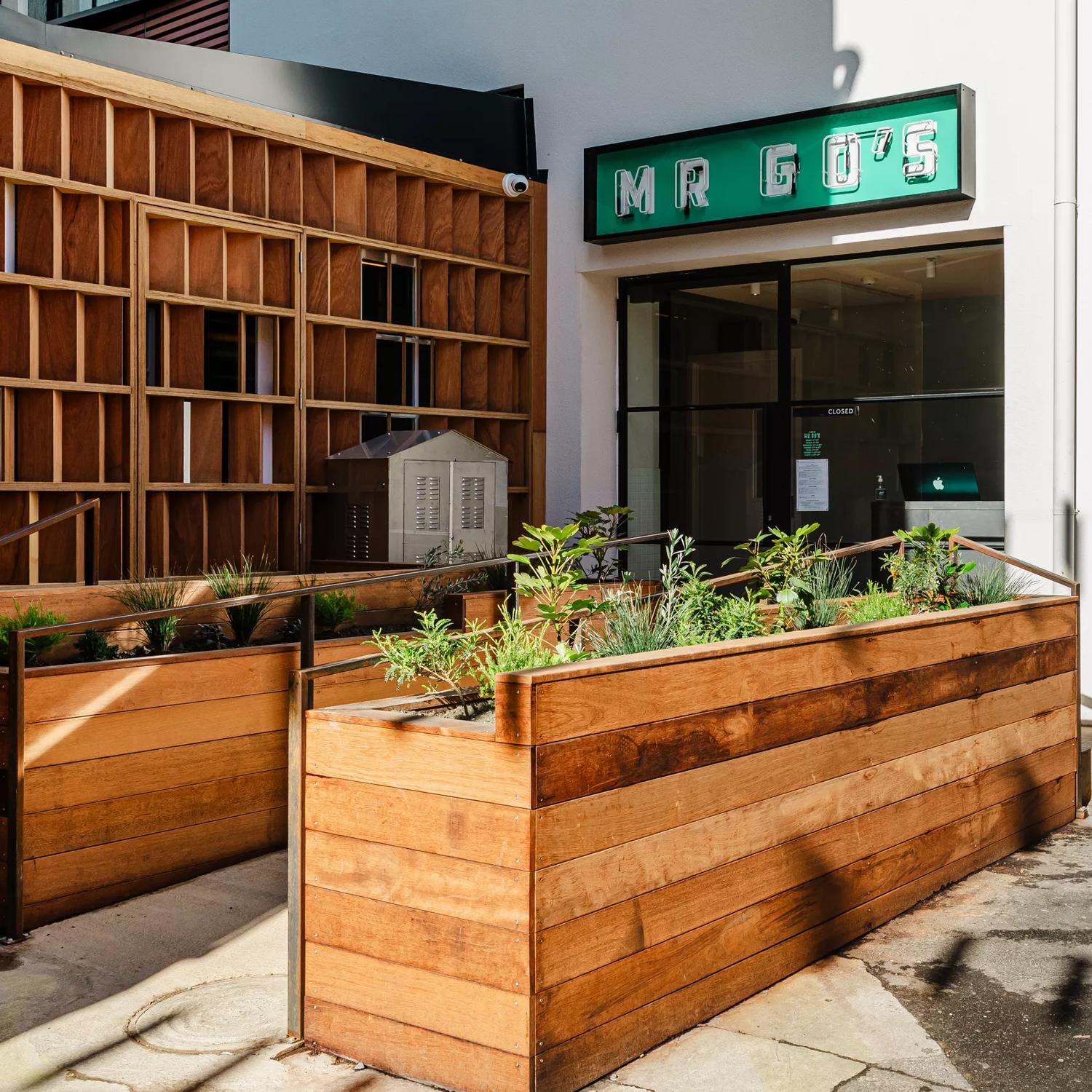 The front door of Mr Go's restaurant located on Eva Street in Wellington's city centre with wooden garden beds, white walls and a green sign.  