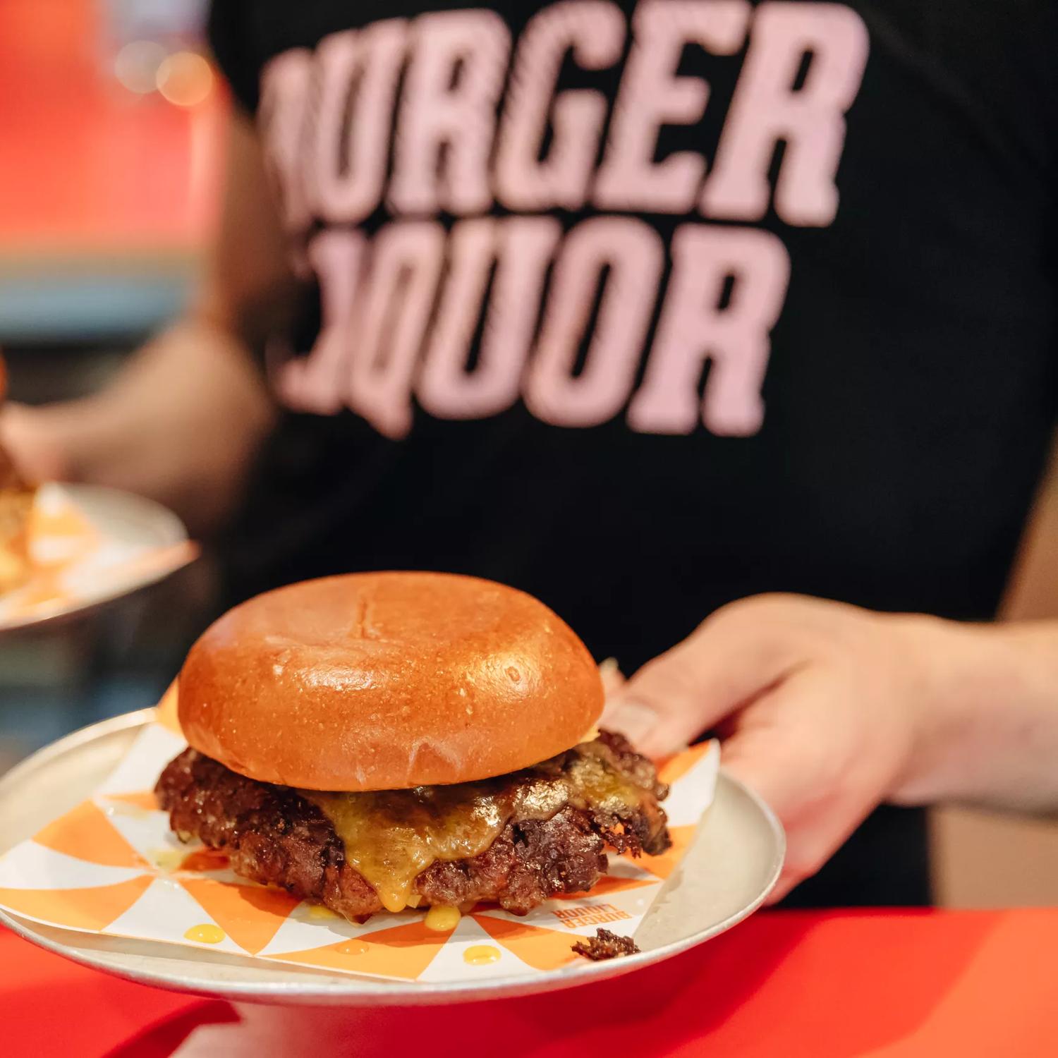 A waiter wearing a black teeshirt with 'Burger Liquor' written on it carries two burgers.