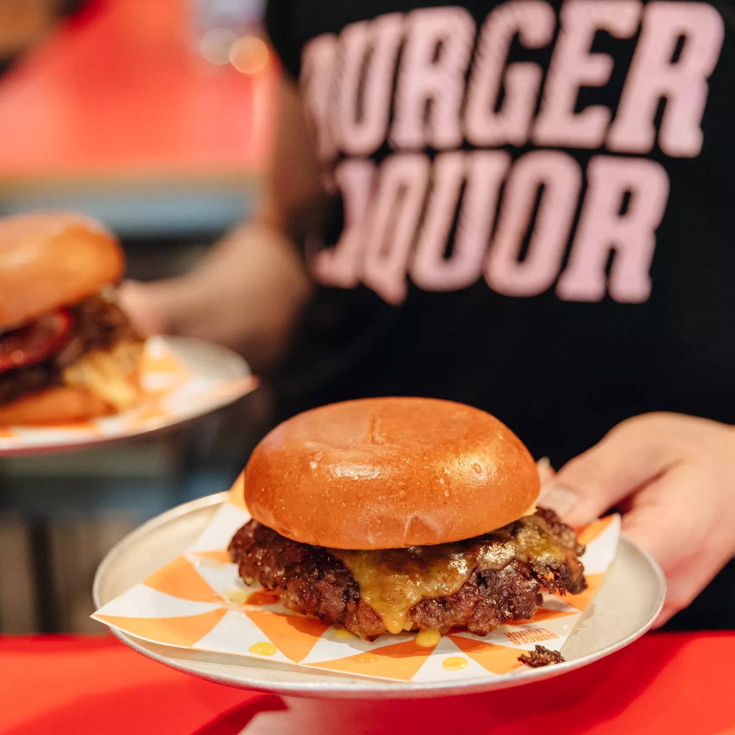A waiter wearing a black teeshirt with 'Burger Liquor' written on it carries two burgers.