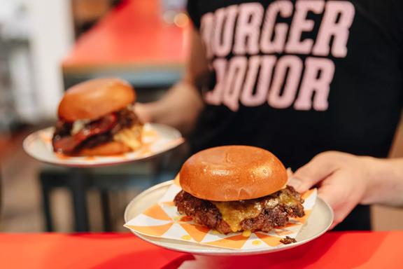 A waiter wearing a black teeshirt with 'Burger Liquor' written on it carries two burgers.
