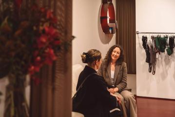 Maxine Kelly, Underlena's Director, sits with someone on a couch inside the lingerie shop.