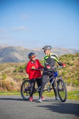 Two adults on a tandem cycle, stopped to talk. They are on the sealed path Te Ara o Whareroa in Queen Elizabeth Park, Kāpiti Coast.