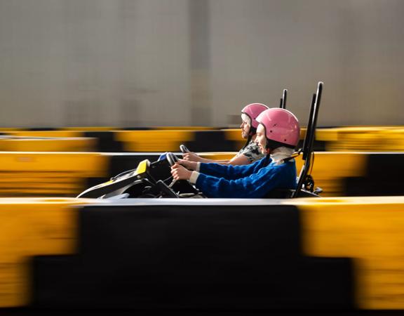 Two people racing in go-karts at Daytona Adventure Park in Upper Hutt. People are in focus whilst the rest of the image is blurred to show speed.