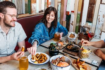 Three people eat crab and other seafood plates at The Crab Shack on Queens Wharf.