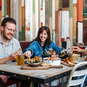 Three people eat crab and other seafood plates at The Crab Shack on Queens Wharf.