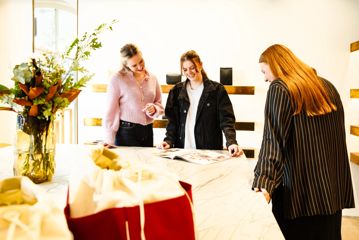 Three people surround the counter at Yu Mei, looking at a magazine.