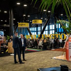 At MEETINGS 2023 at Tākina two people stand in the middle of the venue surrounded by exhibition booths.