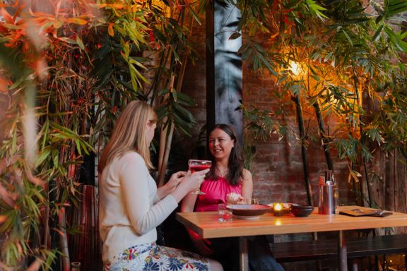 Two friends enjoying cocktails in a courtyard surrounded by bamboo plants.