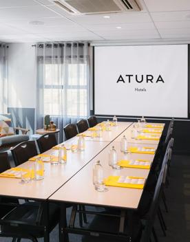 Conference room in Atura Hotels with 12 chairs around a rectangle table and couches in the corner.
