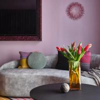 The interior of Naumi Boutique Hotel in Wellington with a black circle coffee table, a light grey irregular shaped couch with four pillows and a small throw blanket and a pale purple wall in the background. 