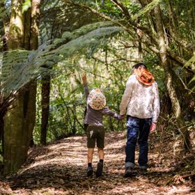A section of trail Te Ara o Tama in Ōtari-Wiltons Bush. A parent and child hold hands and walk along the path as the child points upward.