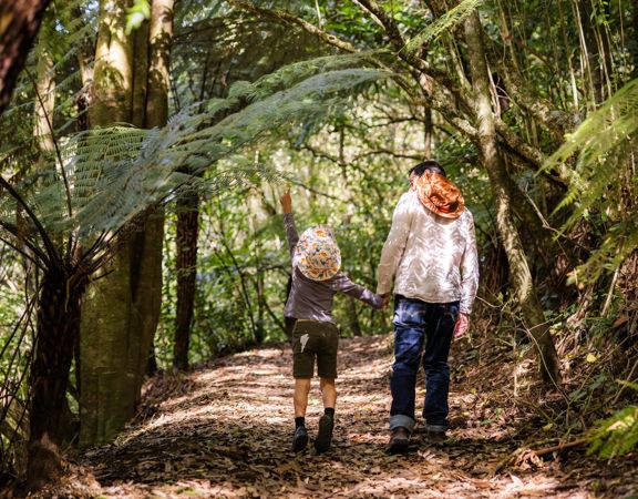 A section of trail Te Ara o Tama in Ōtari-Wiltons Bush. A parent and child hold hands and walk along the path as the child points upward.