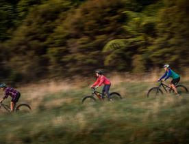 Three cyclists ride down a grassy hill.